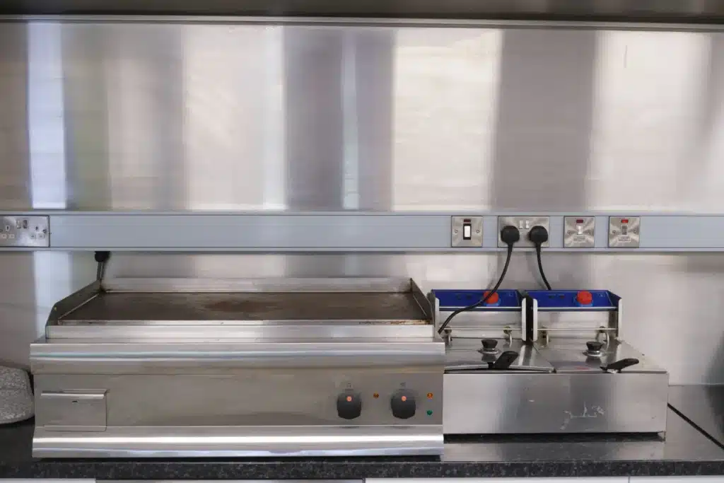 Équipement Cuisine Professionnelle : Griddle et Friteuse Griddle et friteuse double en inox dans une cuisine professionnelle avec prises électriques murales.